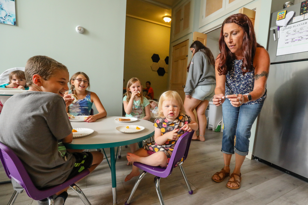 Woman squatting above young children sitting at a table